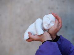 En person håller en vit skulptur av en liggande person i sina händer.