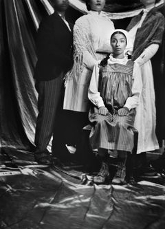 Fyra personer i gammaldags kläder står och sitter i en formell studioinställning.