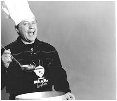 Porträtt av Helge Skoog iklädd en vit köksmössa och svart skjorta med en soppslev i handen.