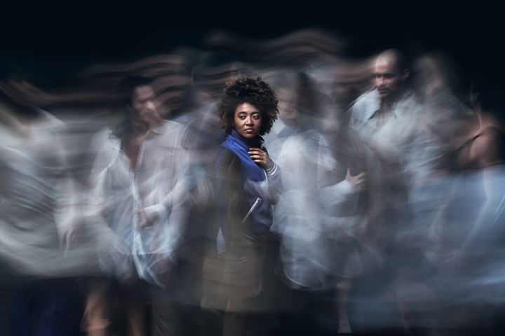 En person står omgivet av suddiga silhuetter av andra dansare i rörelse.