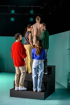 Alt text: Skådespelare står i en trappa på en scen, klädda i avslappnade kläder.