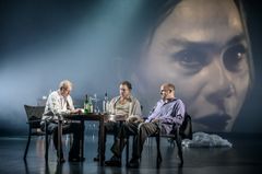 Tre personer vid ett bord och en kvinna syns på en skärm bakom de.