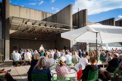 Människor sitter och lyssnar på framträdande på Taket en solig dag.
