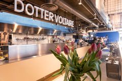 Blomsteruppsättning i fokus framför en disk med skylten "Dotter Voltaire" på Kulturhuset Stadsteatern.