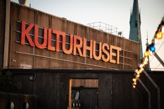 Skylt med texten "Kulturhuset" på en byggnad, med några dekorativa ljus i förgrunden.