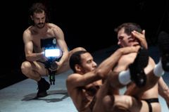 Alt-text: Tre män utför en dramatisk scen på en scen med en kamera.