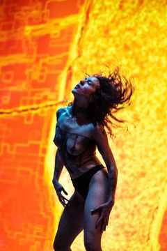 En person poserar framför en livlig, abstrakt bakgrund i varma färger.