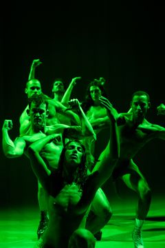 Bild av sju personer som dansar i dramatisk belysning med en grön ton.