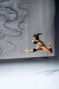 En person hoppar i luften på en scen, med konstnärlig bakgrund.