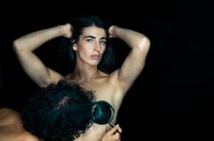 Bild på två personer som förbereder sig för en föreställning. En person håller en svart objektformad rekvisita nära den andra personens bröst.