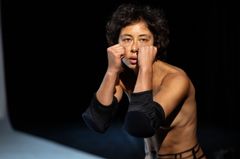 Kvinna i en danspose med armarna upp framför ansiktet på en scen.