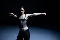 En person utför en dansrörelse i ett mörkt belyst rum.