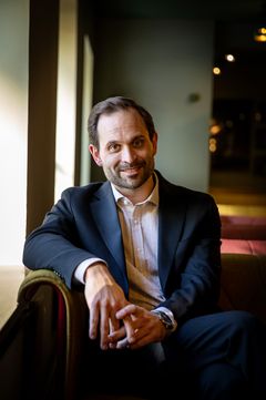 Porträtt på Rikard Lekander sittandes i en soffa vid ett fönster.