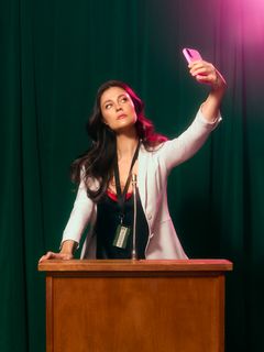 Skådespelare i talarstol som håller upp en mobiltelefon för att ta en bild.