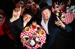 Två män, Helan och Halvdan, i svart kostym och med plommonstop på huvudet som reser sig upp från ett dukat på på Soppteatern.