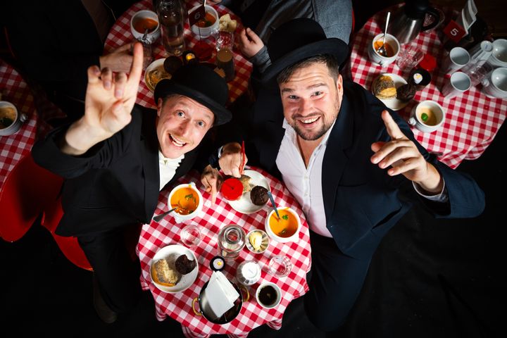 Två män, Helan och Halvdan, i svart kostym och med plommonstop på huvudet som reser sig upp från ett dukat på på Soppteatern.