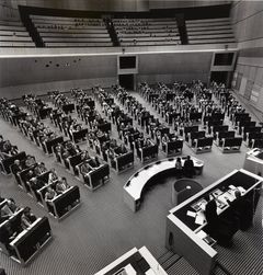 Svartvitt foto av en fullsatt riksdagssal med många personer vid sina platser och en läktare i bakgrunden.