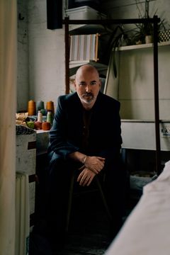 Douglas Stuart sitter inomhus i en kreativ miljö med garnrullar i bakgrunden.