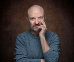 Jonas Gardell i grå tröja poserar mot en brun bakgrund.