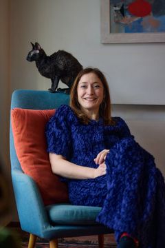 Linda Bondestam sitter leende i en fåtölj med en katt bakom sig på ryggstödet.