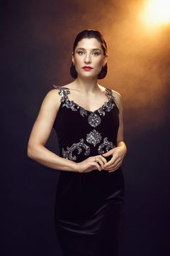 Kvinna i elegant svart klänning med glittrande detaljer, står mot en mörk bakgrund med varmt ljusskimmer.