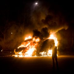 En skåpbil står i brand och en person syns fotografera händelsen.