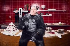 En rökande man i gorilladräkt som sitter på ett mjöligt bord i bagerimiljö