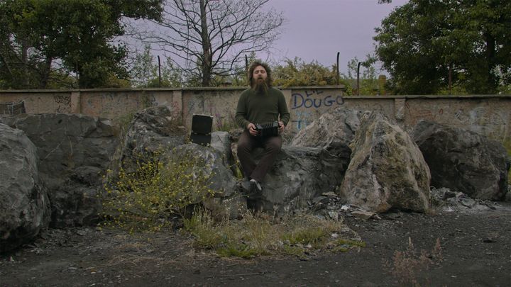 En man sitter utomhus och spelar dragspel och sjunger