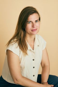 Porträtt av Annakarin Thorburn med långt brunt hår och ljus skjorta, sittande mot en beige bakgrund och vänd mot kameran.