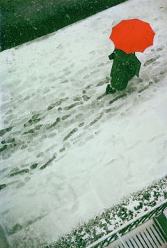 En person med ett klarrött paraply går över en snötäckt mark, fotograferad snett ovanifrån.