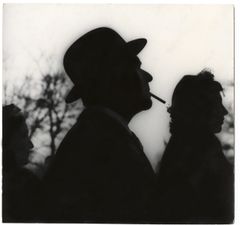 Svartvitt fotografi av människor i silhuett. I mitten syns en man i hatt med en cigarett i munnen.