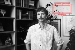 Svartvitt porträtt av Aron Landahl med mustasch och randig skjorta framför bokhyllor. Uppe till höger syns logotypen för Kulturhuset Stadsteaterns Bilderbokspris.