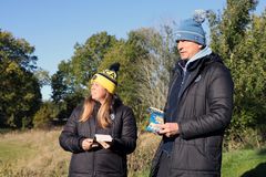 Två golftränare, en kvinna och en man, står på en golfbana en vacker höstdag. De håller varsitt block med banguide.