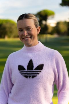 Kvinna i ljuslila tröja med svart Adidas-logotyp står utomhus med en grönskande bakgrund.