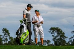 Två personer på en golfbana; en kvinnlig caddie och en manlig golfspelare pratar och går tillsammans.