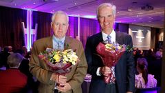 Två män med blommor står bredvid varandra under en prisceremoni.