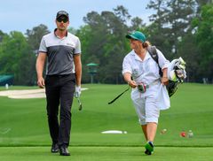Bild på en man och en kvinna som går på en golfbana, där kvinnan är caddie och bär golfklubbor.