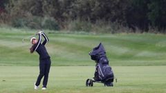 En juniortjej svingar en golfklubba på fairway. Bredvid henne står en golfbag.