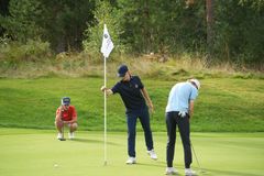 Tre juniorkillar spelar golf. En puttar, en kollar puttlinje, en håller flaggan.