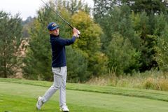 Tonårig golfspelare slår ett slag på en grön golfbana omgiven av träd.