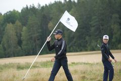 Två unga golfare går över en golfbana, en av dem bär en flagga med Svenska Golfförbundets logotyp.