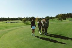 Fyra kvinnor står tillsammans på en golfbana och pratar, med grönt gräs och träd i bakgrunden.