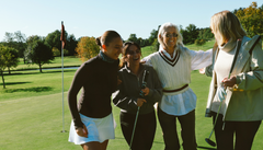 Fyra kvinnor skrattar och kramar varandra på en golfbana.