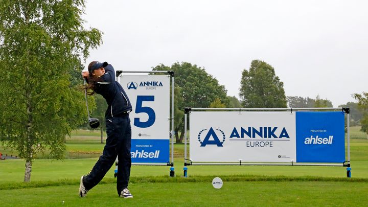 Golfspelare i färd med att slå ett slag på en golfbana, med skyltar för ANNIKA Invitational Europe och Ahlsell i bakgrunden.