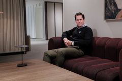 En person sitter på en mörkröd soffa i ett modernt och stilrent rum.