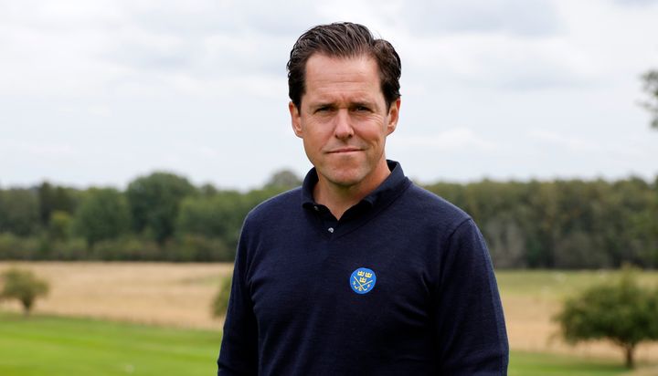 En man som står på en golfbana i en mörkblå tröja med SGF-logotyp.