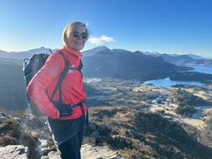 Jenny Ljungberg står på toppen av ett berg klädd i solglasögon och en röd funktionsjacka. Foto.