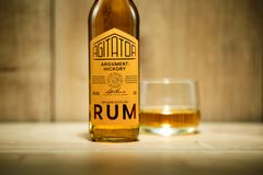 En flaska rom märkt "Agitator Argument: Hickory" står bredvid ett glas med rom.