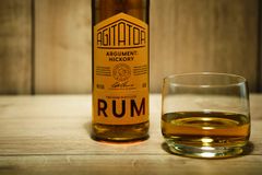 Flaska med etikett "Agitator Argument: Hickory Rum" bredvid ett glas med gyllene rom.