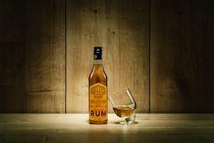 Flaska med rom och ett lutande glas innehållande rom på ett träbord.